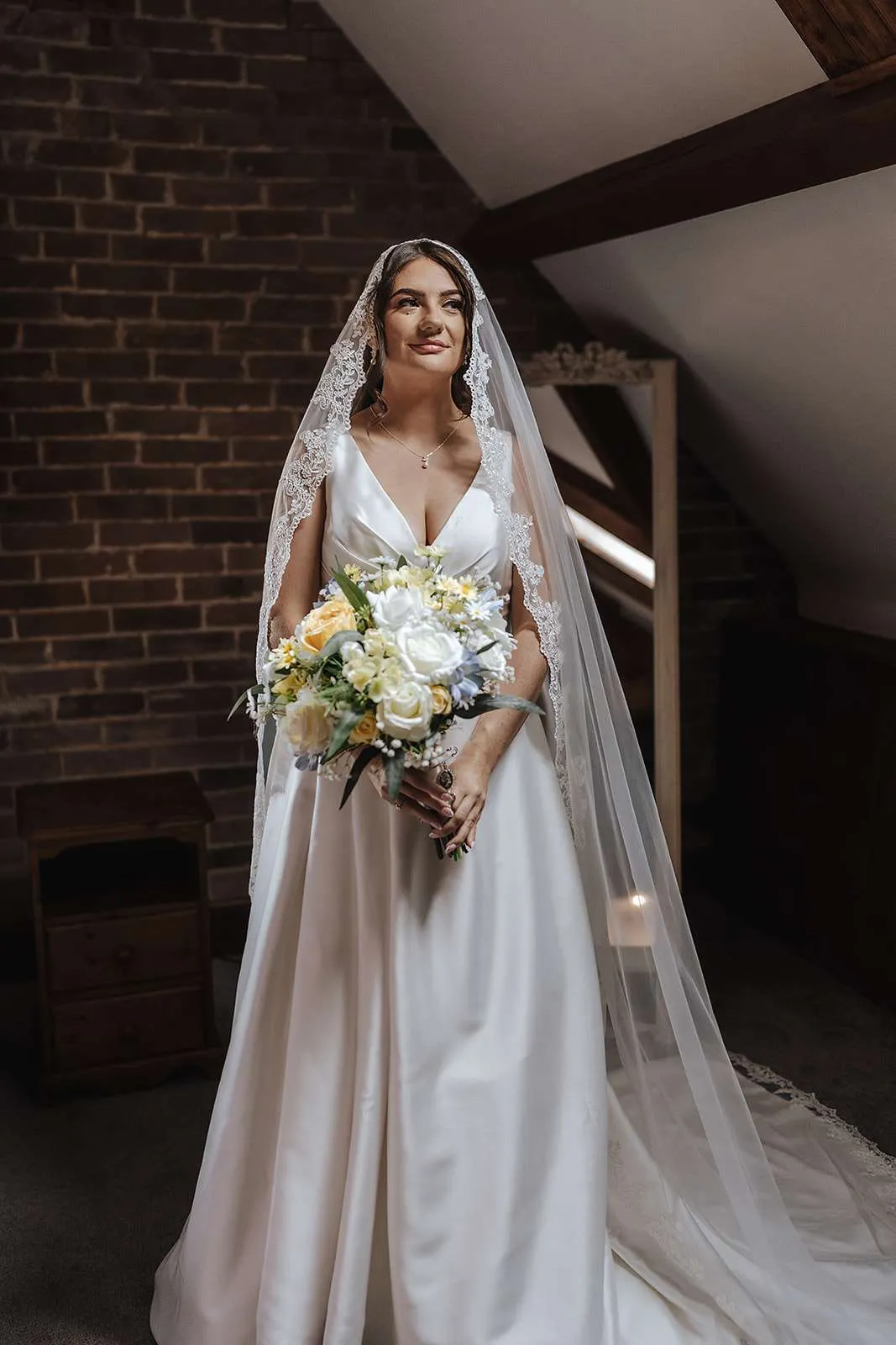 Bride in a long veil holding a white, yellow and pale blue bouquet