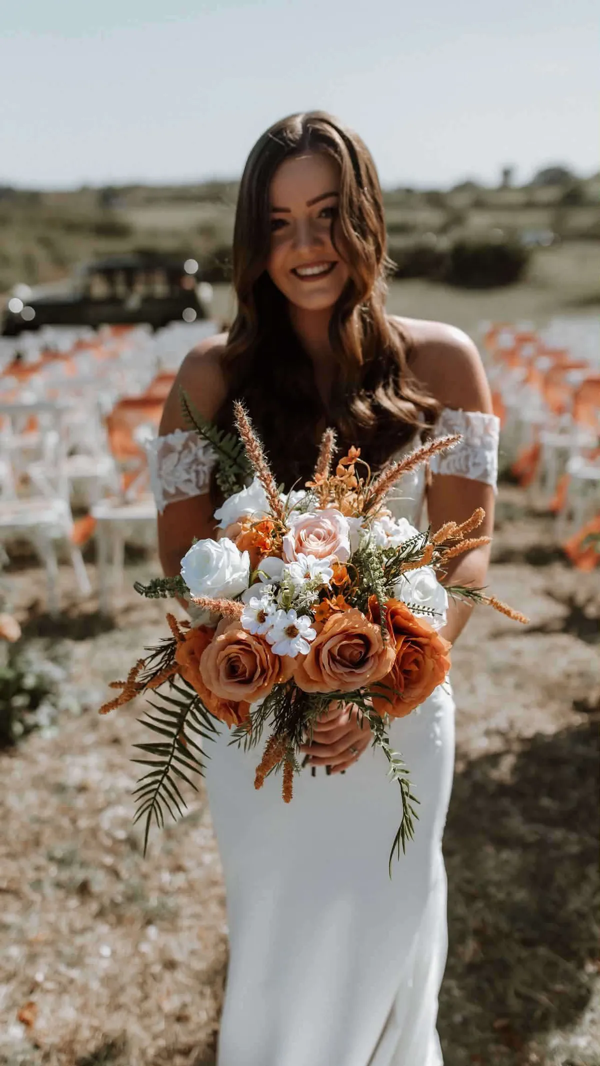 Bride holding a loose bouquet of burnt orange, peach and white blooms with dried grasses