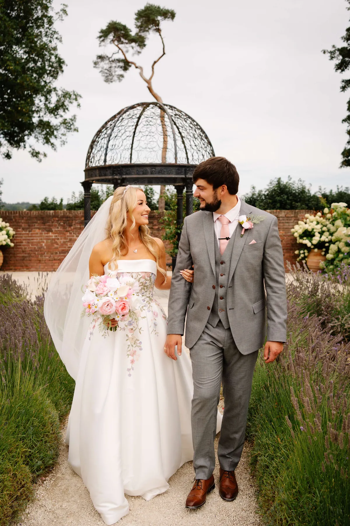 Couple walking from a gazebo, the bride holding a blush bouquet