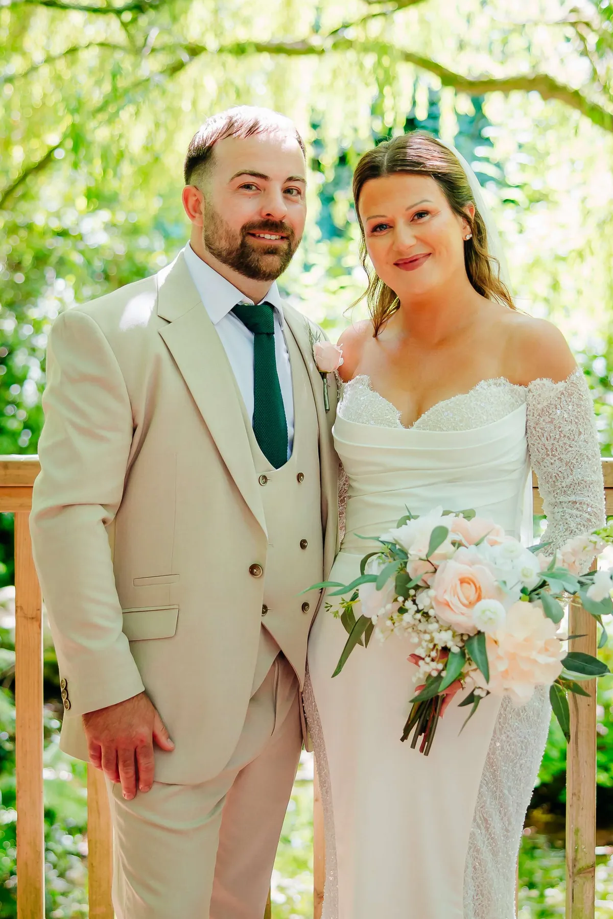 Couple smiling in a garden, the bride holding a blush and white bouquet