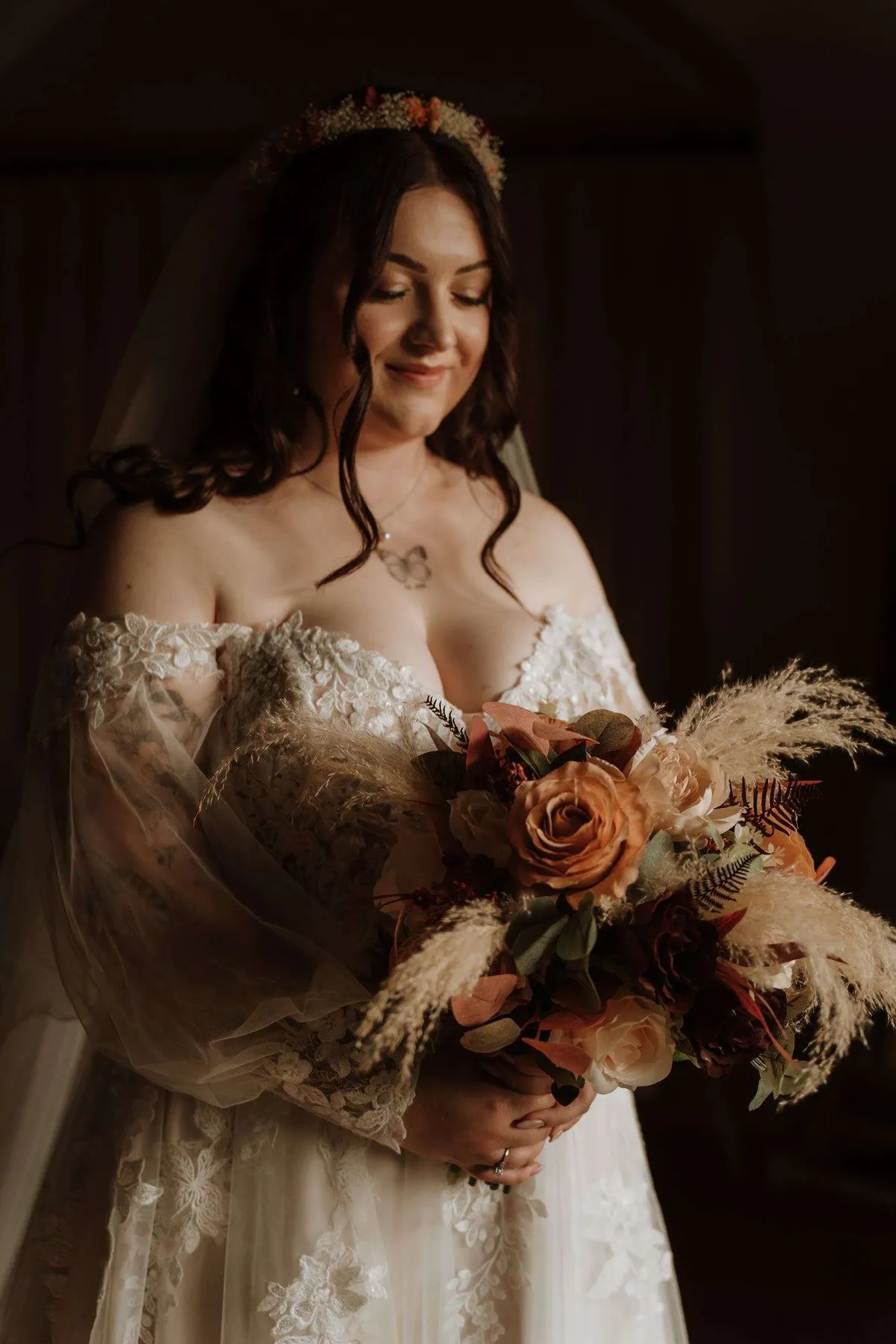 Bride in a lace dress holding an autumnal bouquet with pampas, in moody light