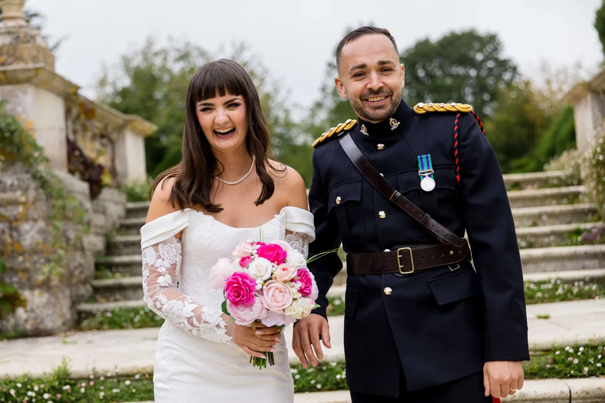 Bride holding a bouquet of hot pink and white peonies beside her groom in military dress