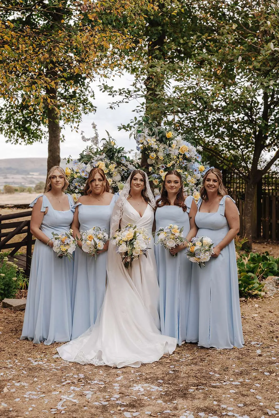 Bride with four bridesmaids in pale blue, all holding white, yellow and blue bouquets