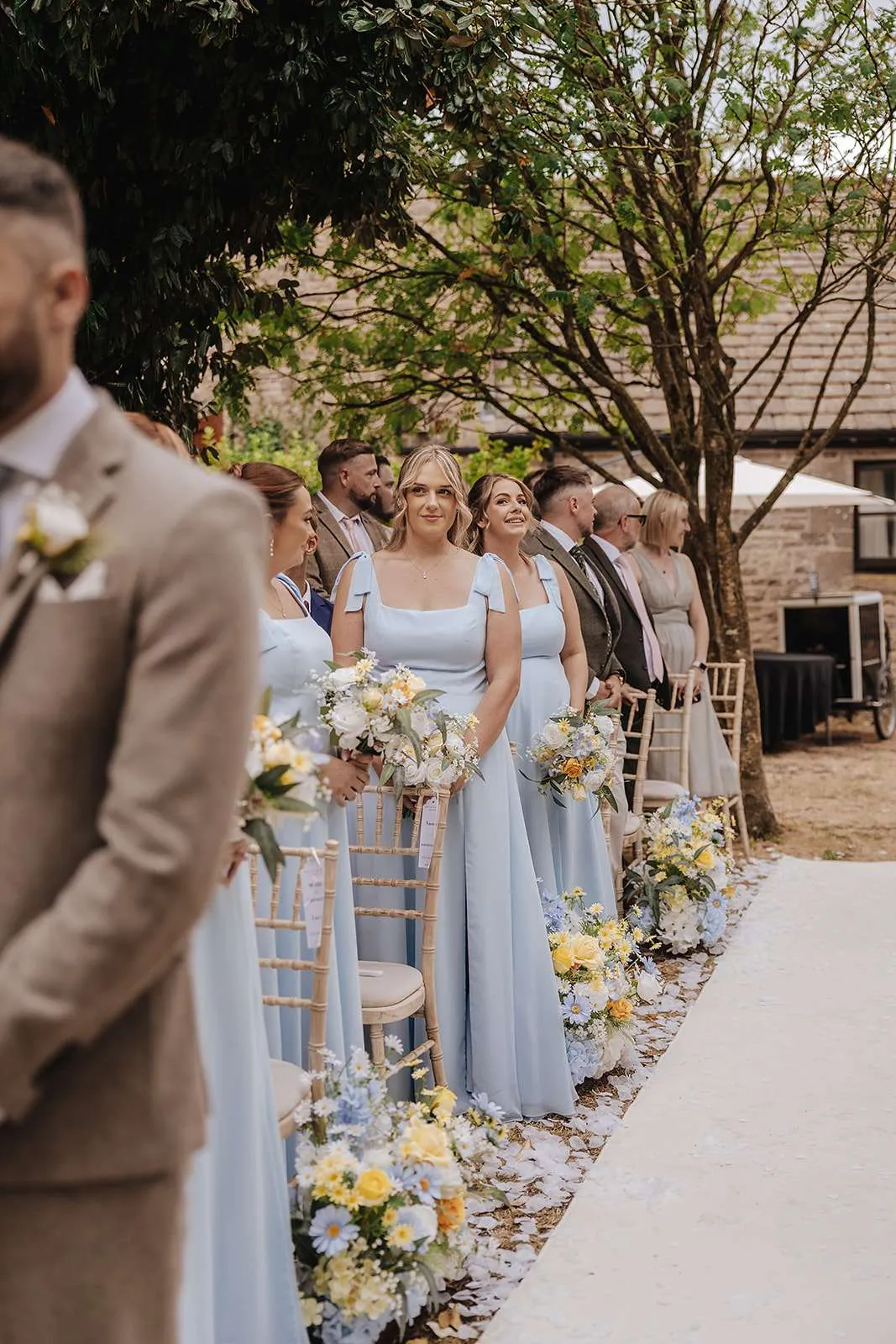 Bridesmaids in pale blue holding bouquets at an outdoor ceremony