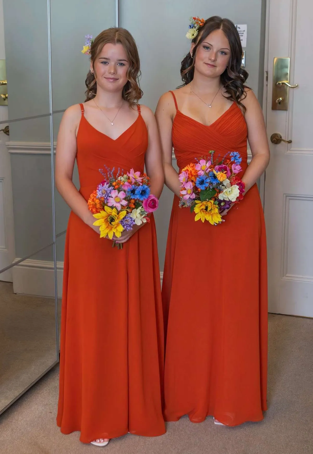 Two bridesmaids in burnt orange dresses holding bright, colourful bouquets