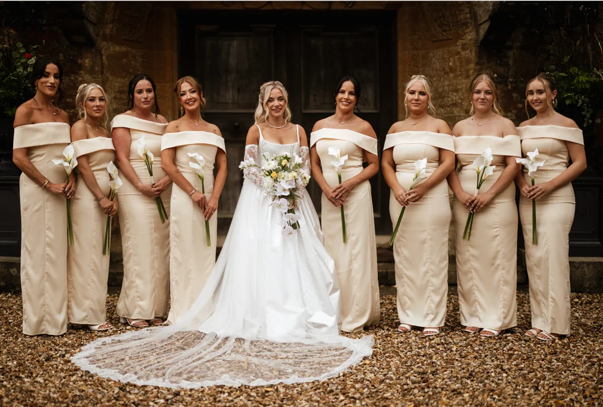 Bride with eight bridesmaids in champagne off-shoulder dresses, each holding a single white calla lily