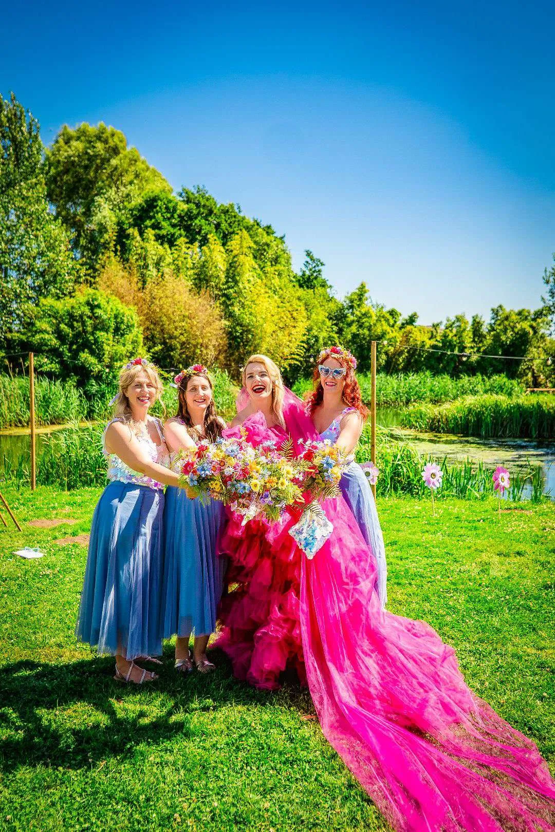 Bride in bright pink with her bridesmaids in blue, all holding colourful bouquets