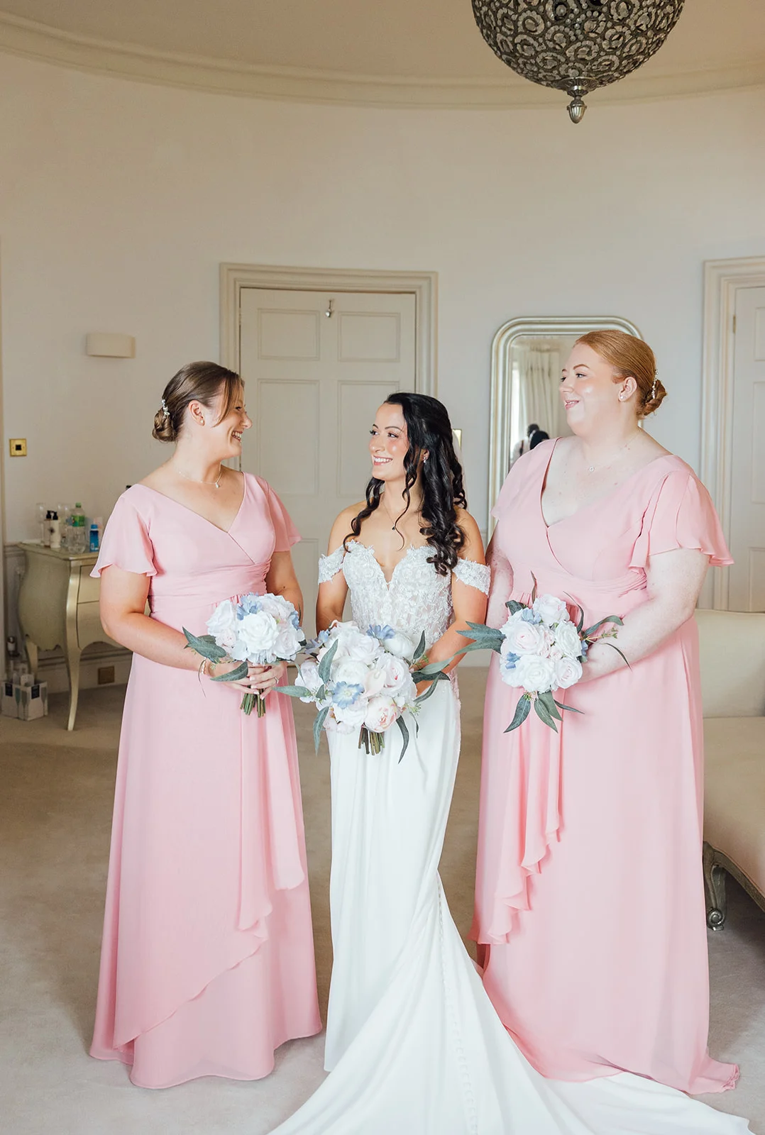 Bride with two bridesmaids in blush pink dresses, all holding white, blush and pale blue bouquets