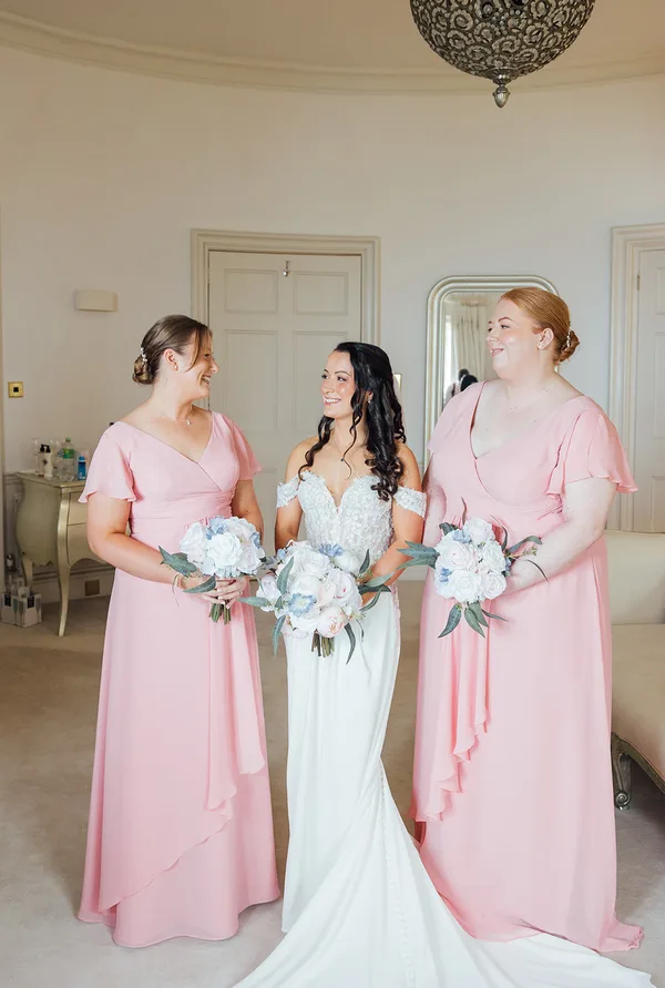 Bride with two bridesmaids in blush pink dresses, all holding white, blush and pale blue bouquets