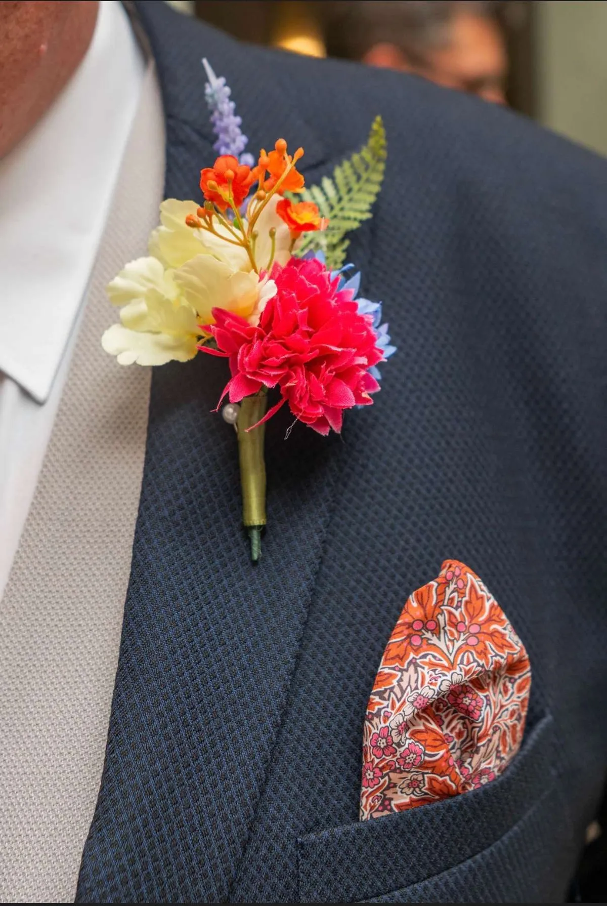Close up of a bright buttonhole of pink, orange and yellow blooms on a navy suit lapel