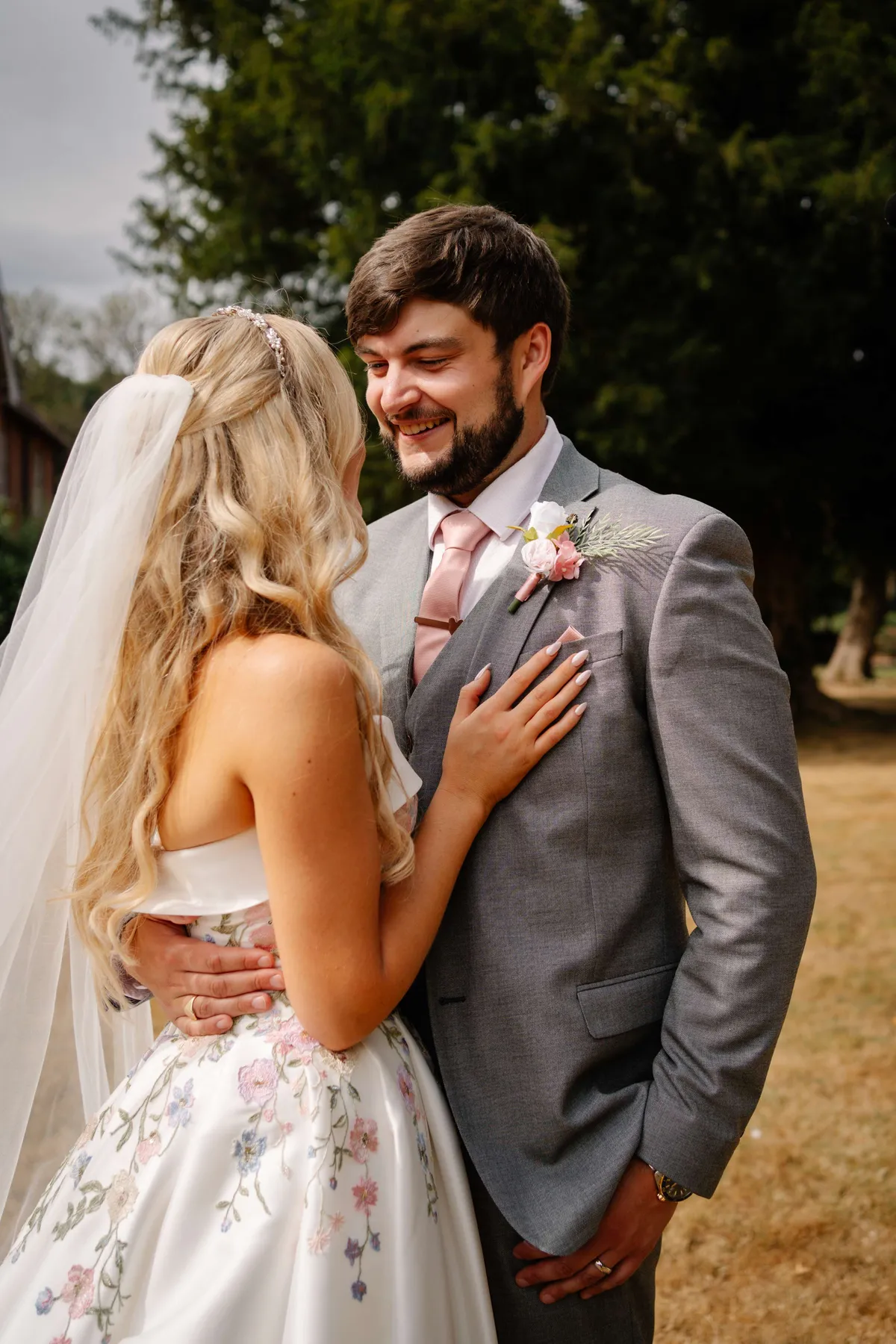 Groom in a grey suit with a blush buttonhole, embracing the bride