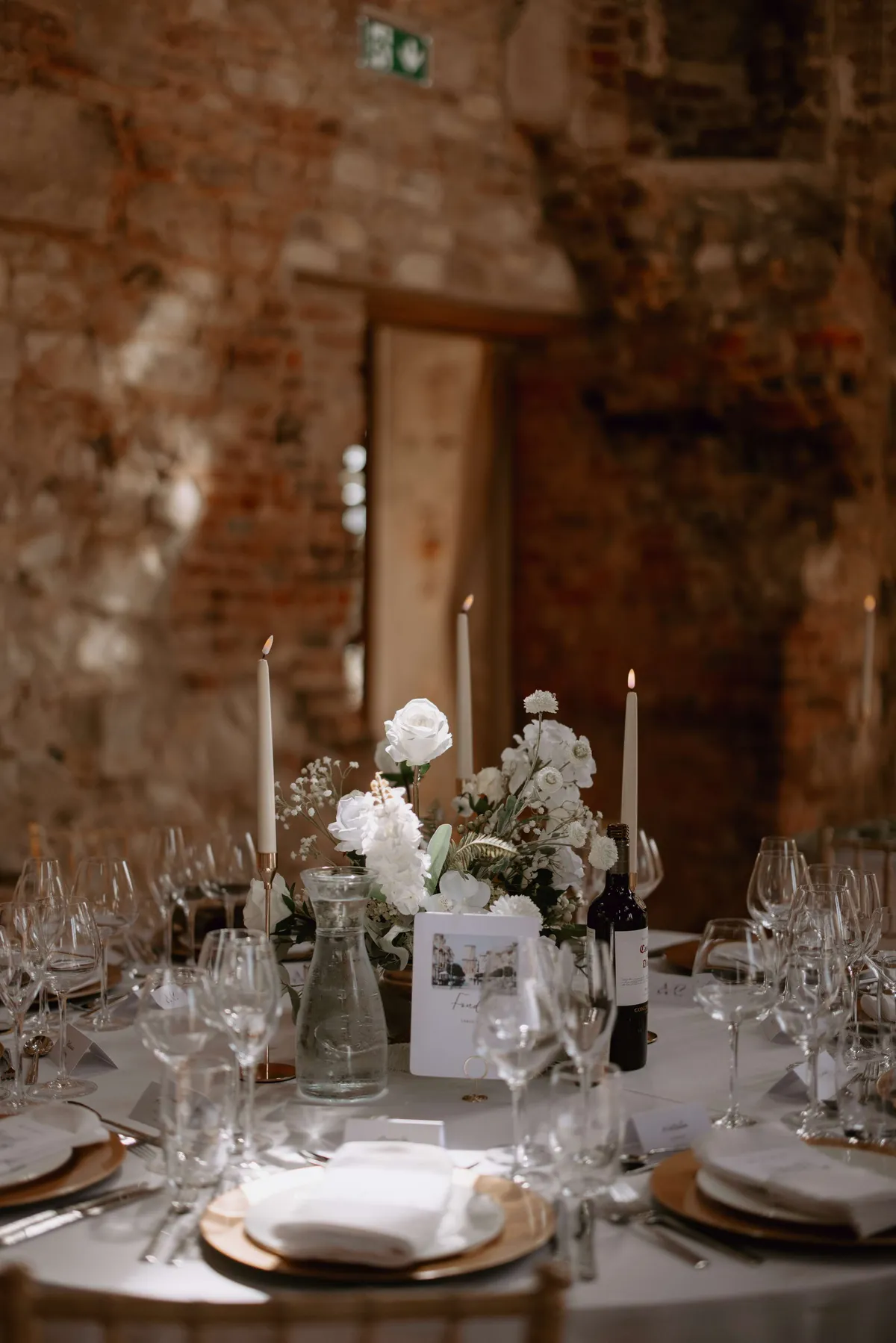 Candlelit round table with a white footed bowl arrangement in a stone and brick hall
