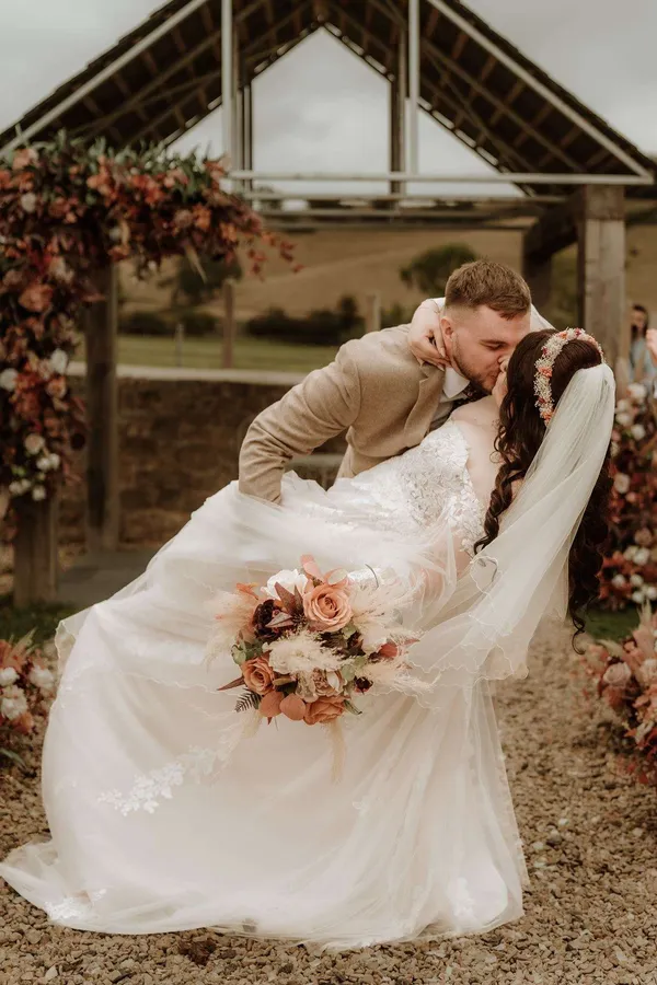 Couple kissing beneath an oak arbor dressed with autumnal florals