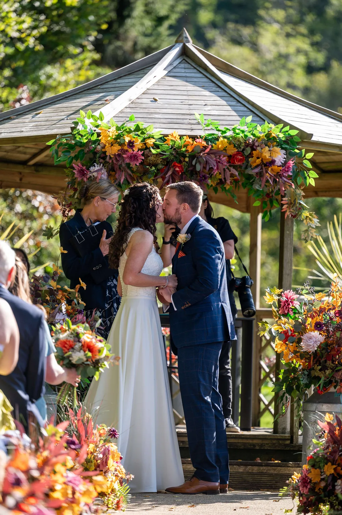 Couple kissing beneath a gazebo dressed with a garland of bright, colourful florals