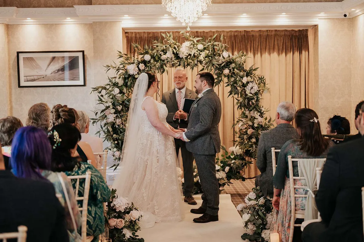 Couple exchanging vows beneath a floral moongate at an indoor ceremony
