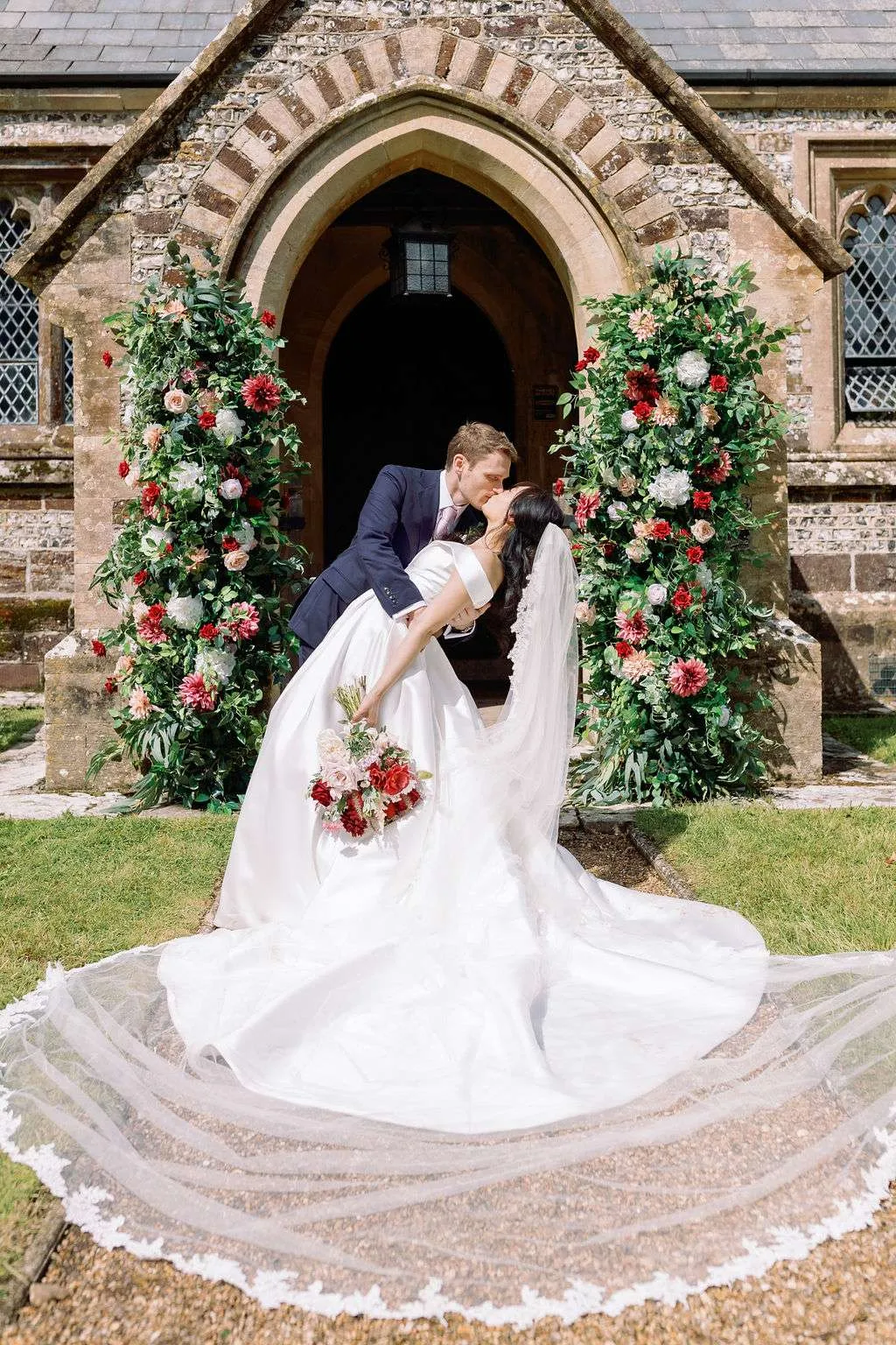 Couple kissing in a church doorway between pillars of pink and red blooms