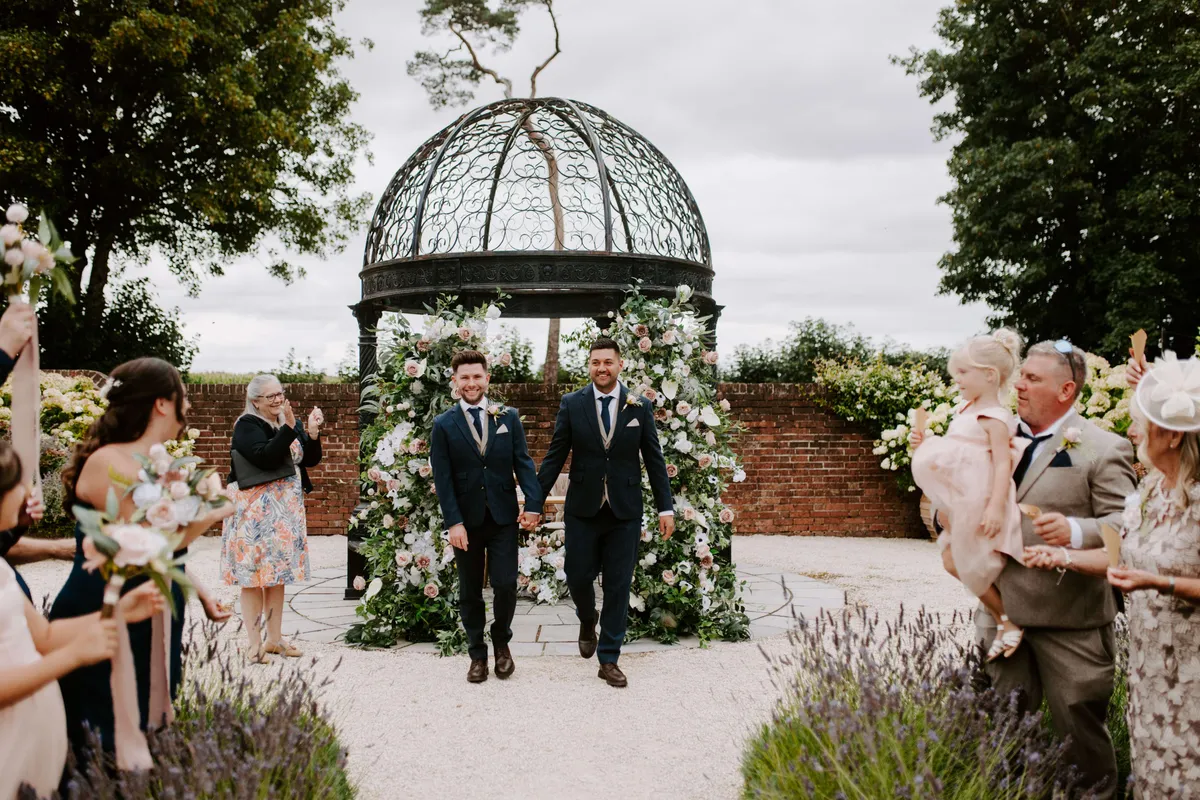 Grooms walking back down the aisle from a gazebo framed by floral pillars