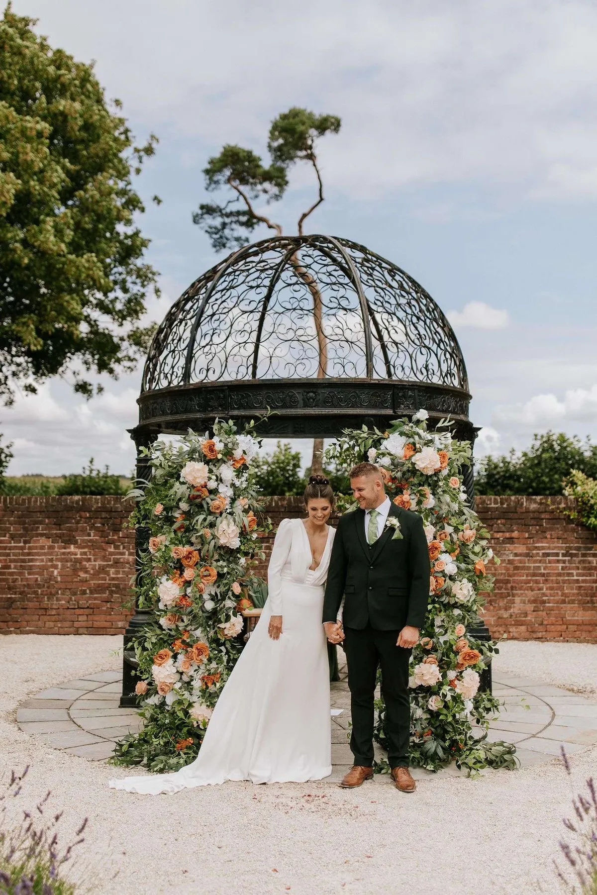 Couple beneath a wrought iron gazebo framed by peach and white floral pillars