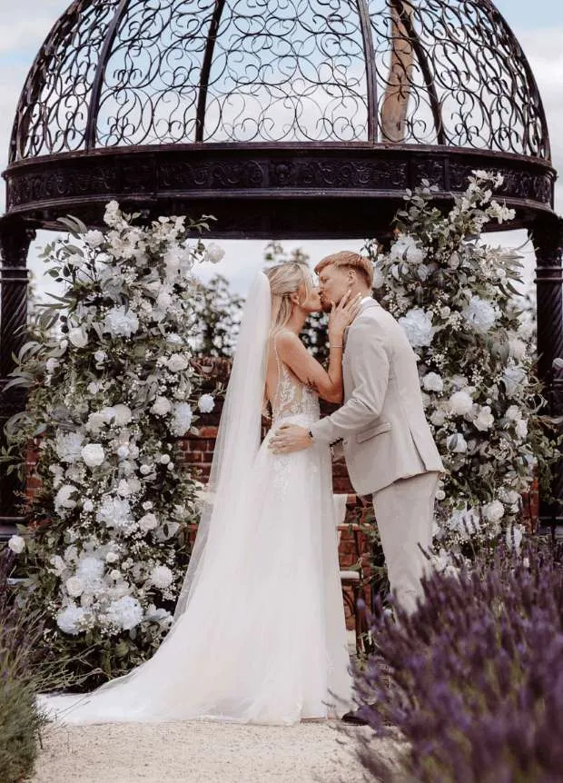 Couple kissing beneath a gazebo between white and blue floral pillars