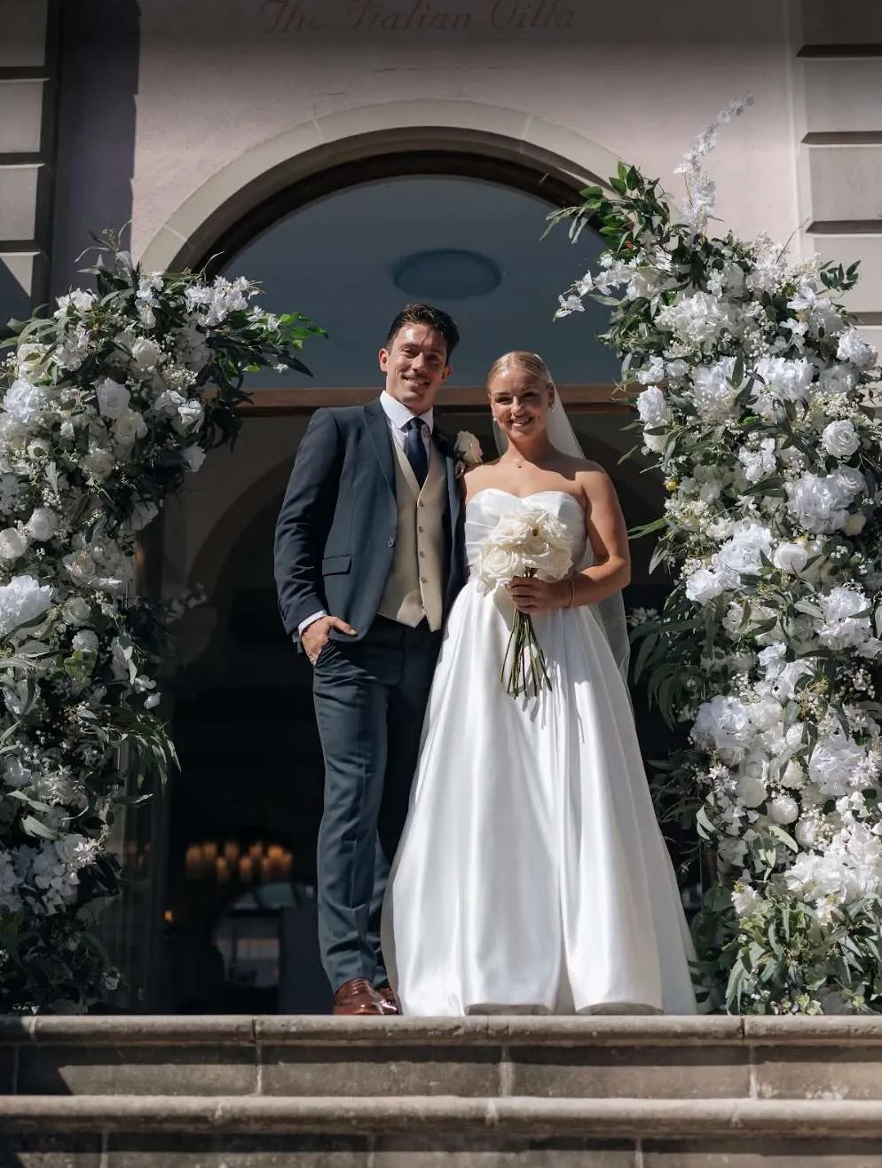 Couple on stone steps between lush white floral pillars
