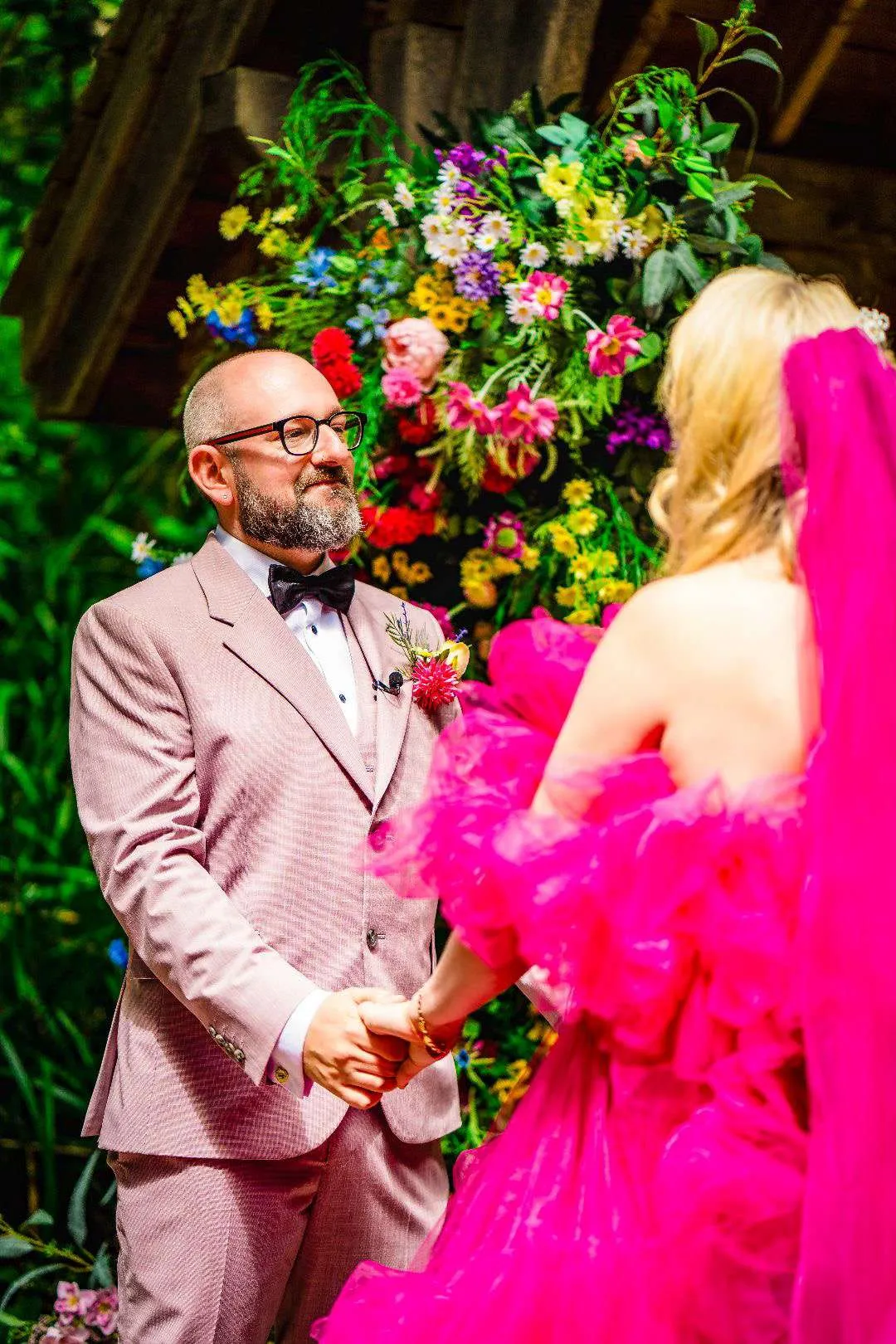 Couple at Rudge Farm in front of a wall of bright, colourful florals