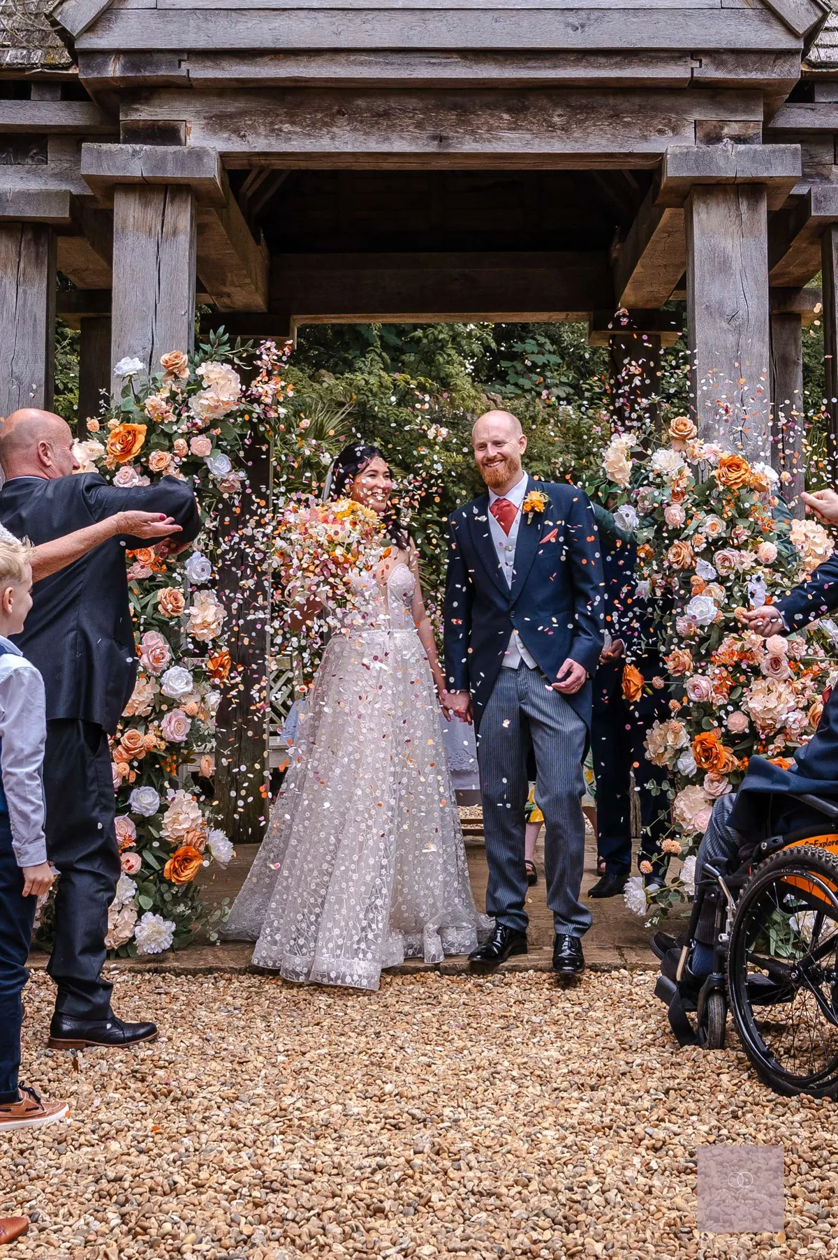 Couple beneath a wooden gazebo at Abbotsbury Subtropical Gardens, framed by peach and white floral pillars