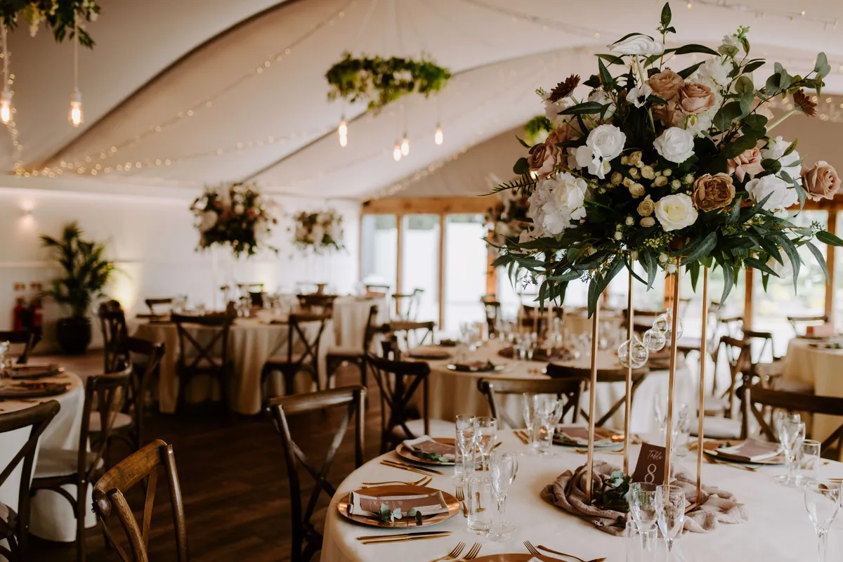 Tall podium arrangement of white and blush blooms on a round table in a marquee