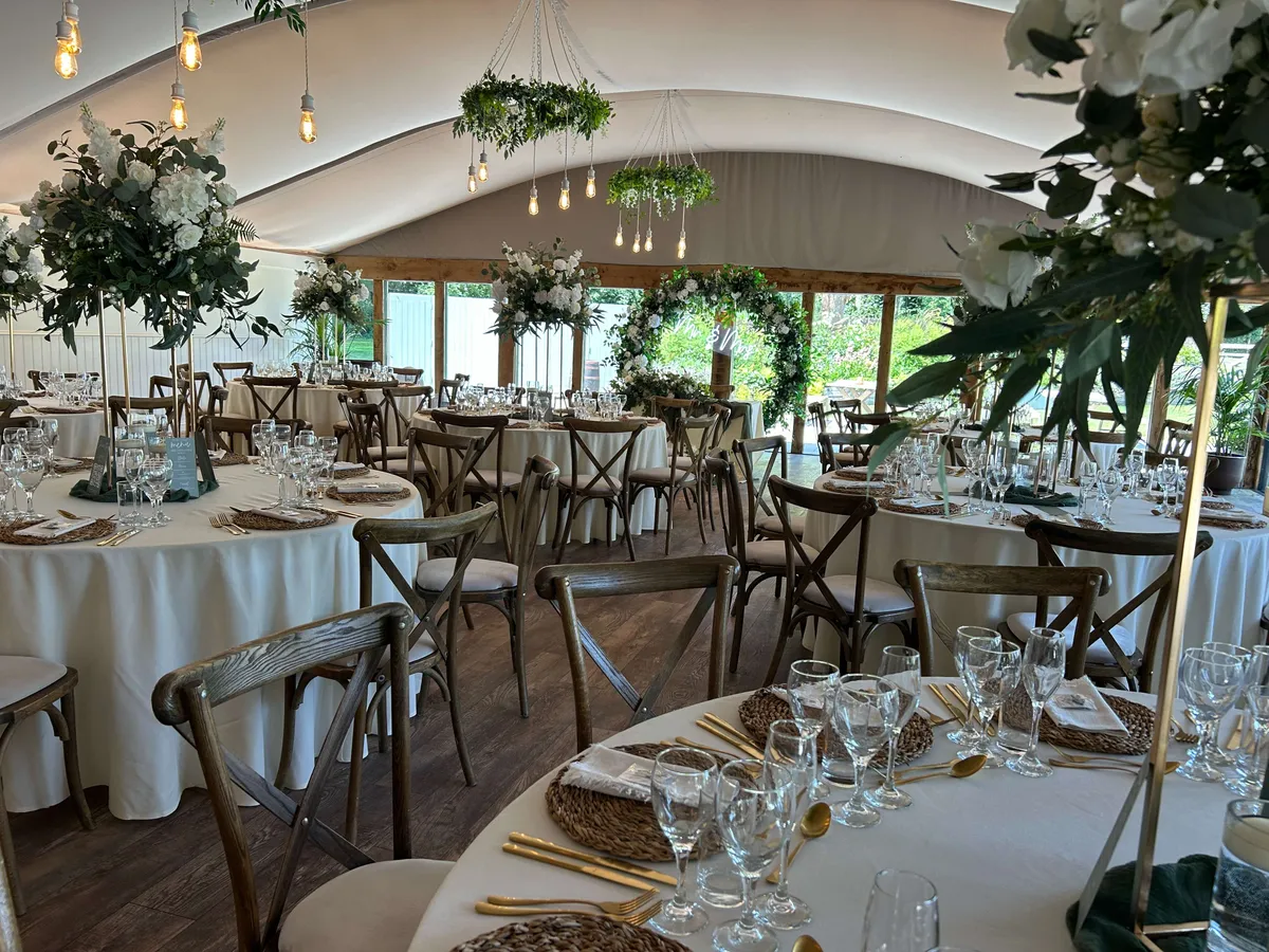Marquee reception with tall podium arrangements and hanging greenery above round tables