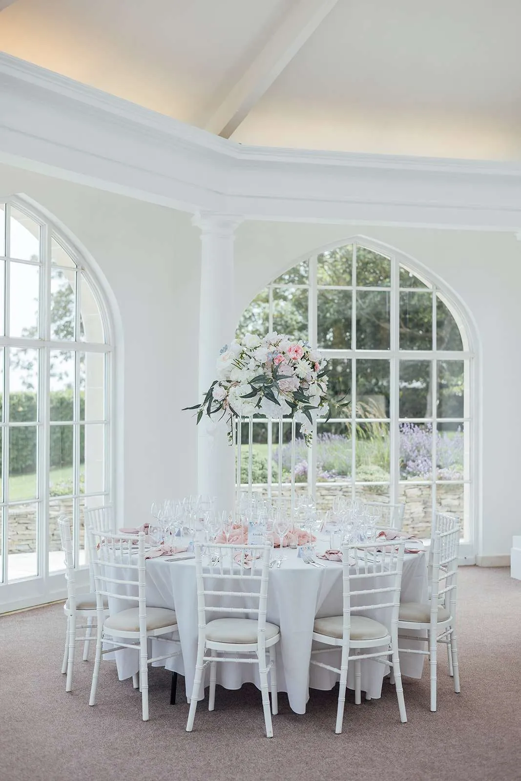 Round table set beneath a tall pastel podium arrangement in a bright white room