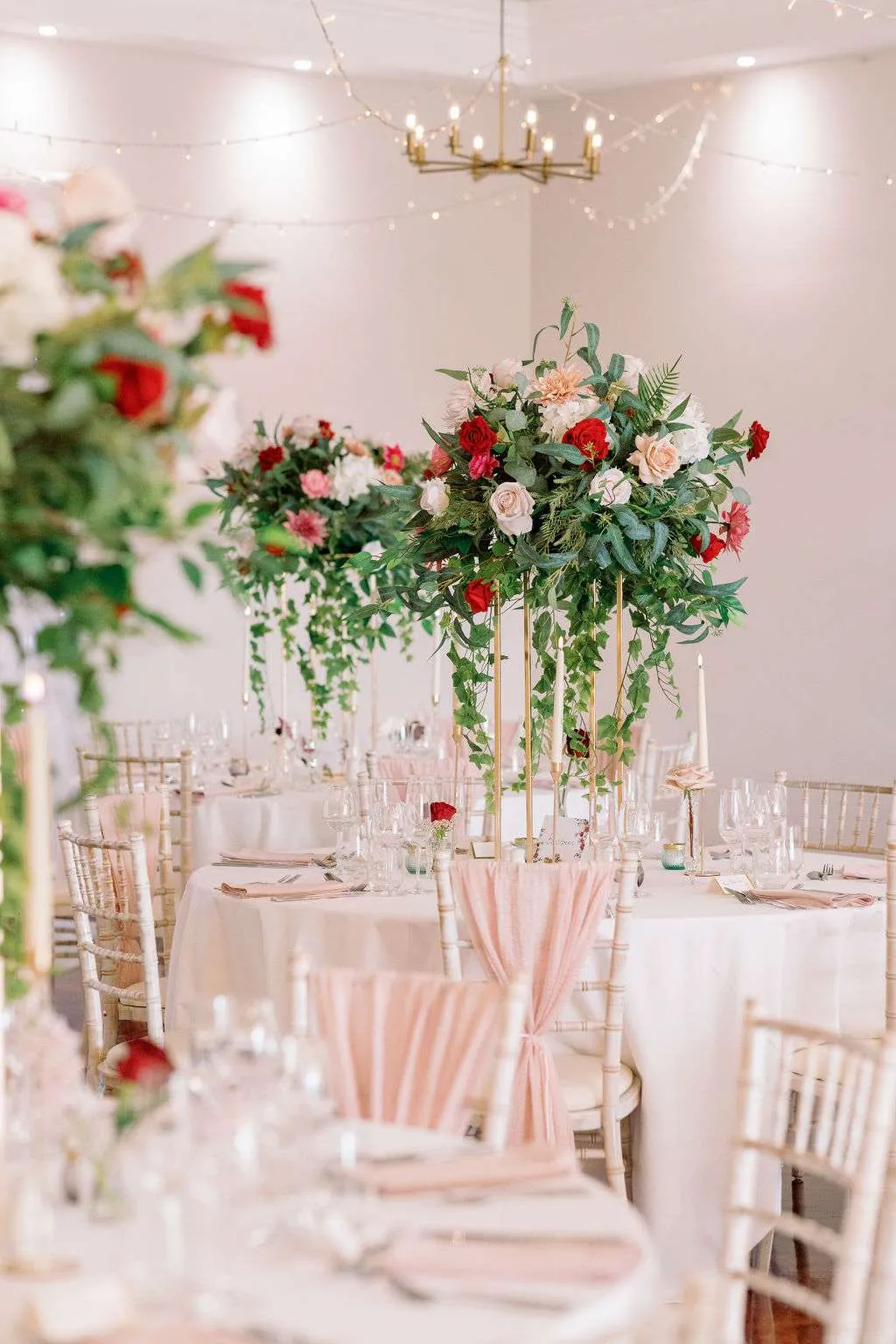 Tall podium arrangement of red, pink and white blooms above a round table
