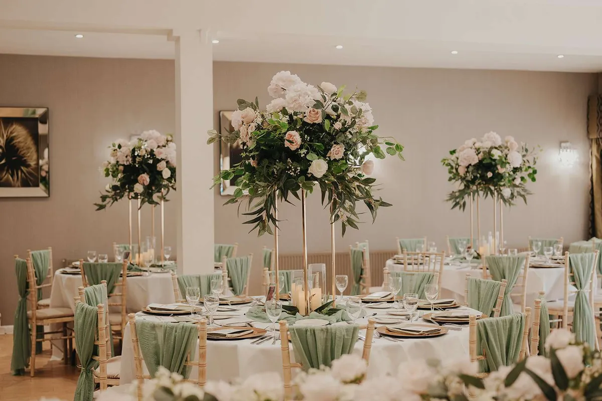 Reception room with tall white and green podium arrangements above round tables and sage chair sashes