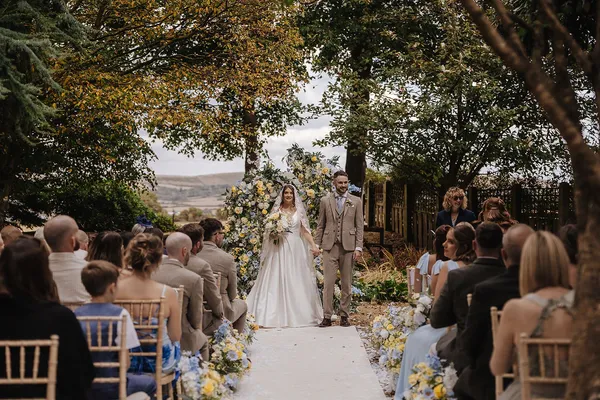 Couple walking back down a garden aisle lined with blue and yellow meadow florals