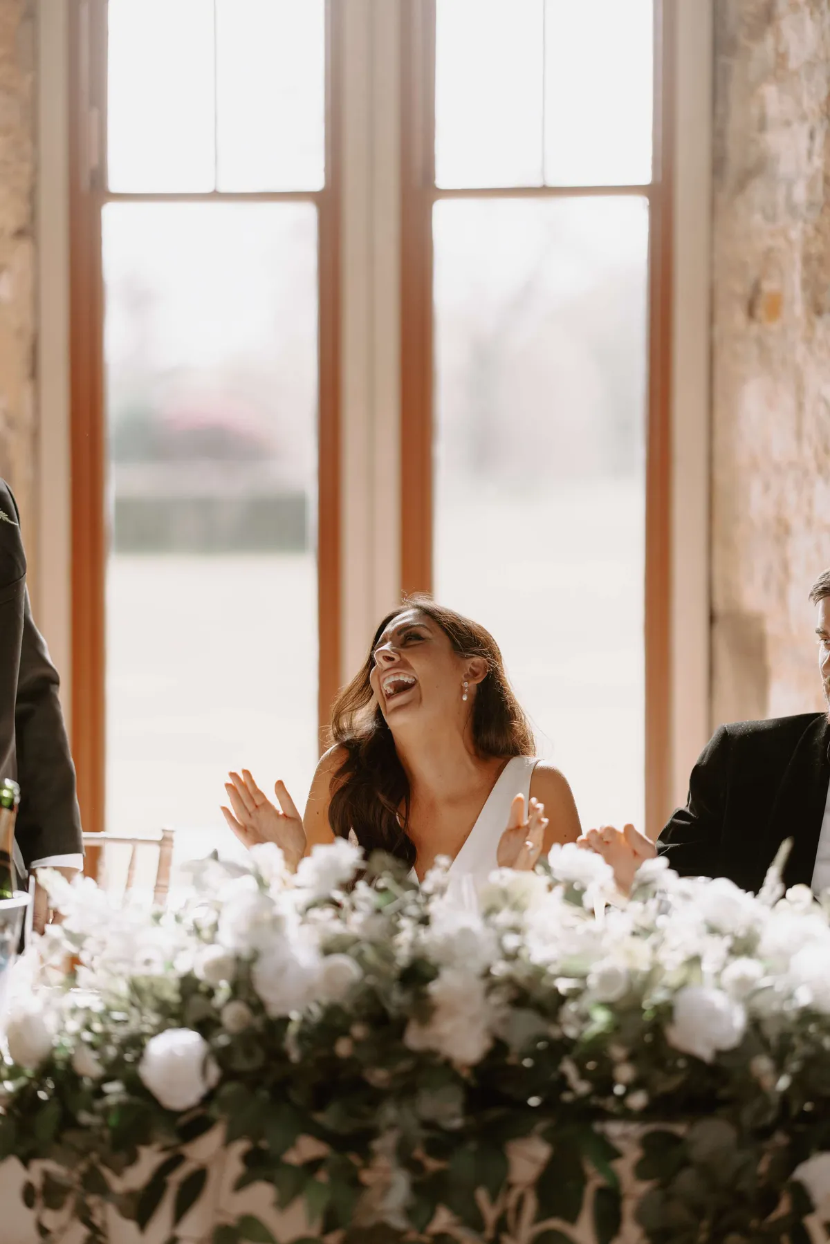 Bride laughing at a top table dressed with white florals and greenery