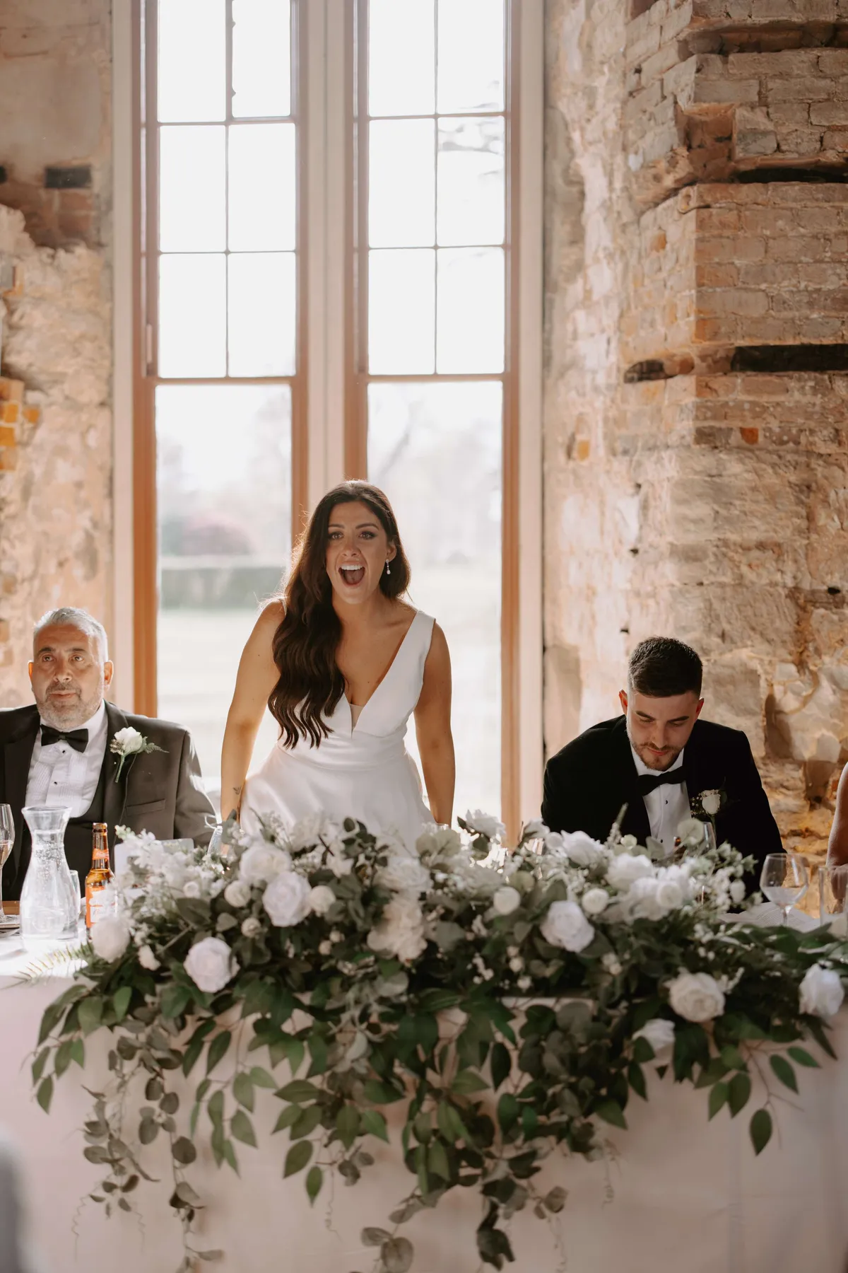 Couple at a top table dressed with a long garland of white blooms and greenery
