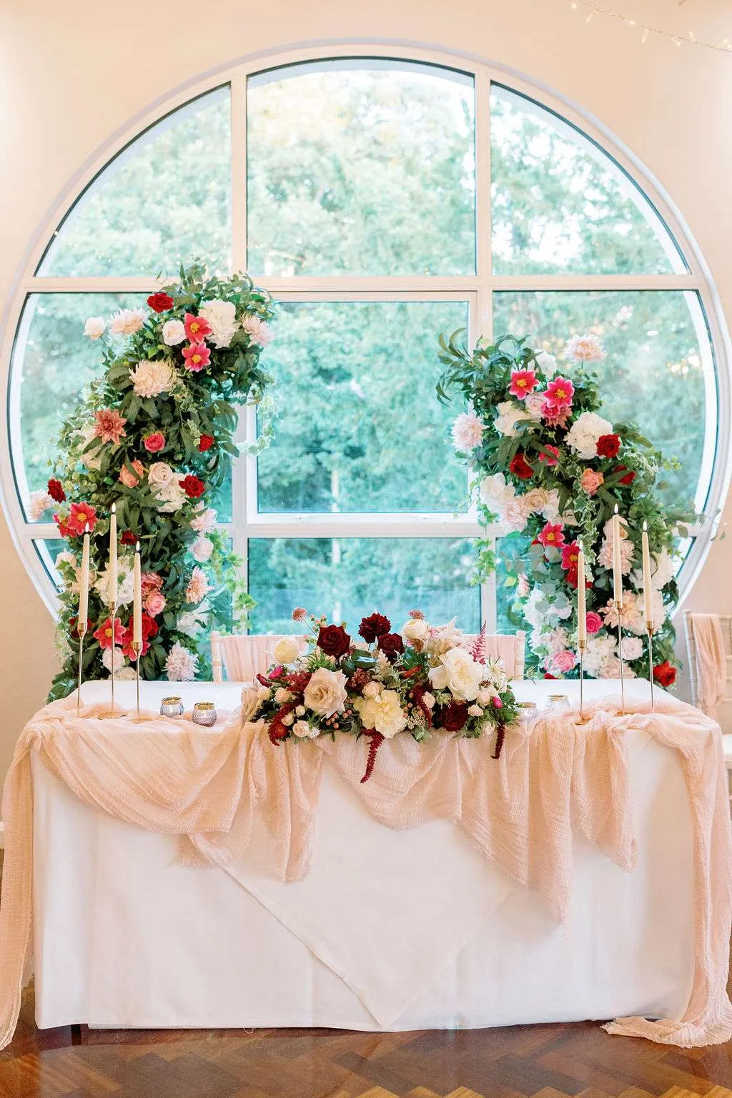 Top table with a pink and red floral arrangement, framed by floral pillars in front of a round window