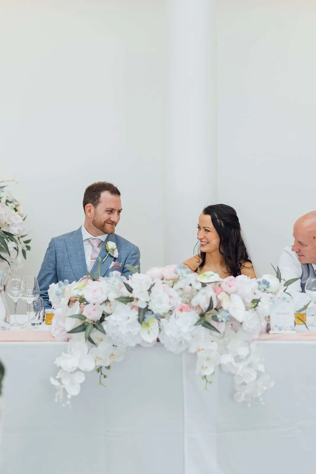 Sophie and Ben at their top table behind white and blush florals