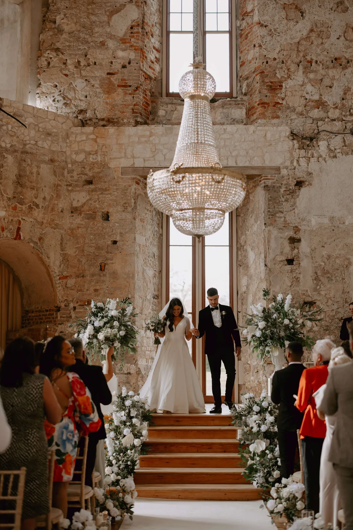 Aisle at Lulworth Castle lined with white floral urns, leading to a grand chandelier