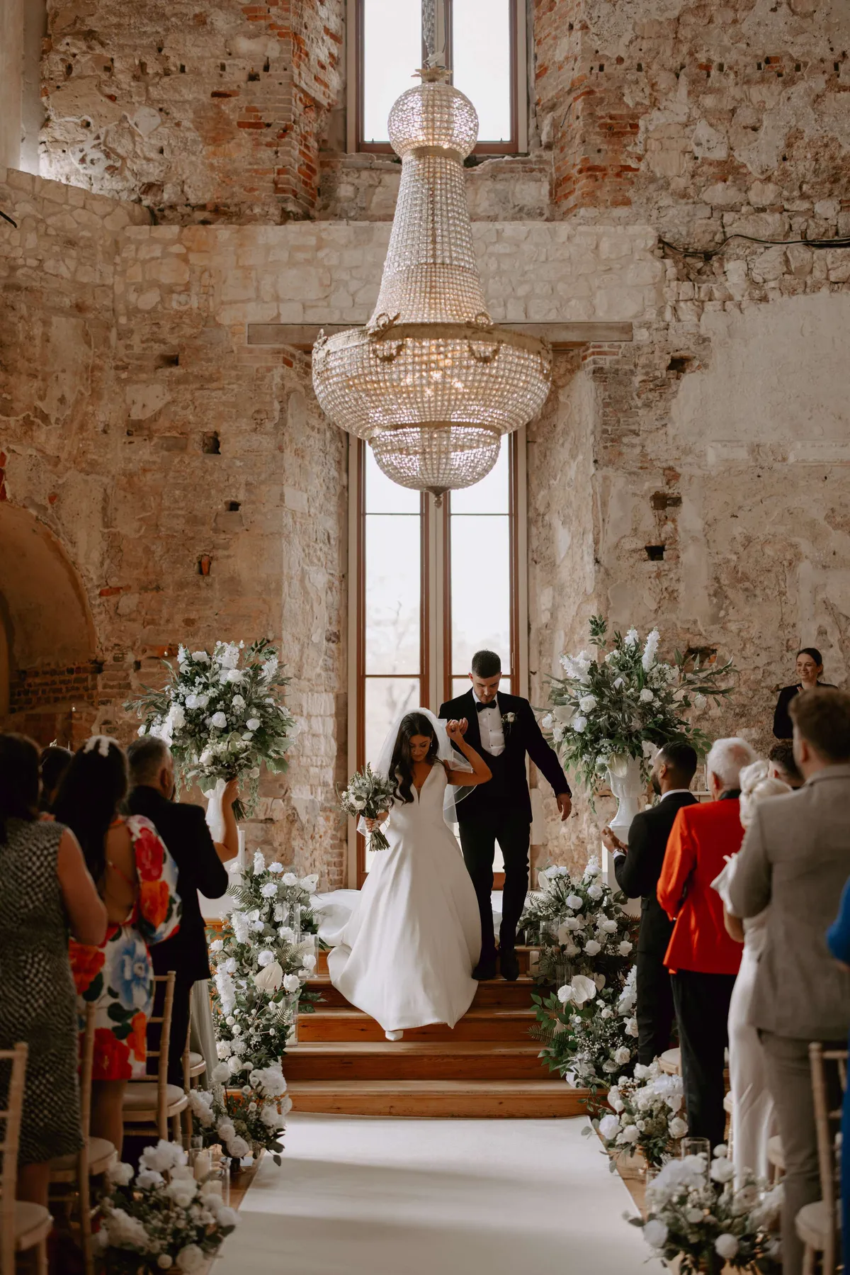 Couple walking back down the aisle at Lulworth Castle between white floral urns