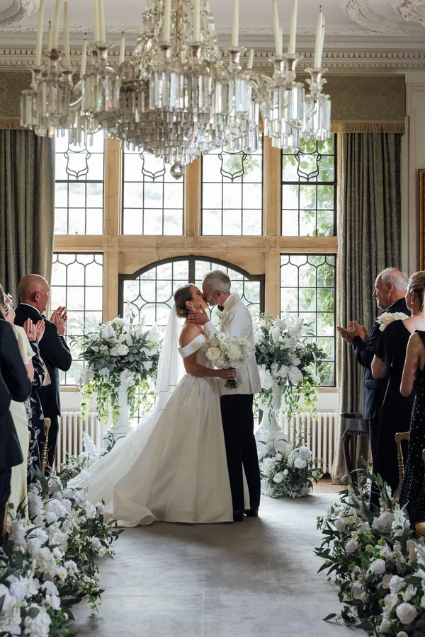 Couple kissing at Minterne House between white floral urns on plinths, beneath a crystal chandelier