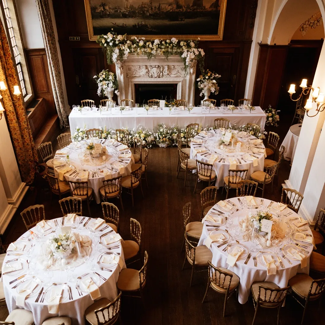 Reception at Minterne House from above: round tables with gold chairs, white florals along the top table and a floral mantelpiece