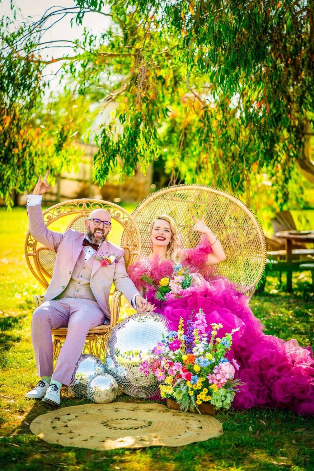 Couple on peacock chairs on a round jute rug, with disco balls and a bright meadow arrangement