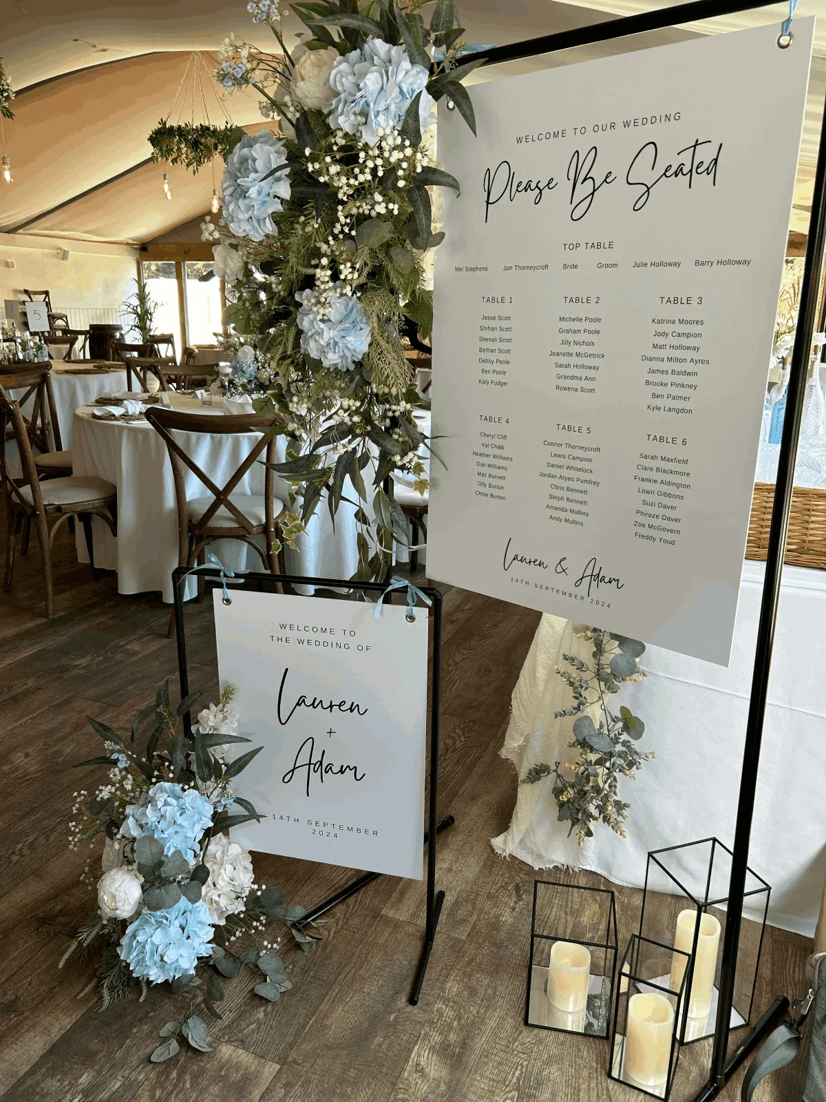 A printed table plan in a black metal frame, with a smaller sign and blue and white florals